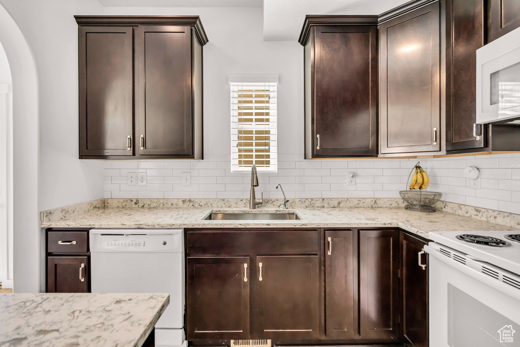 Kitchen with a sink, white appliances, decorative backsplash, and dark brown cabinetry