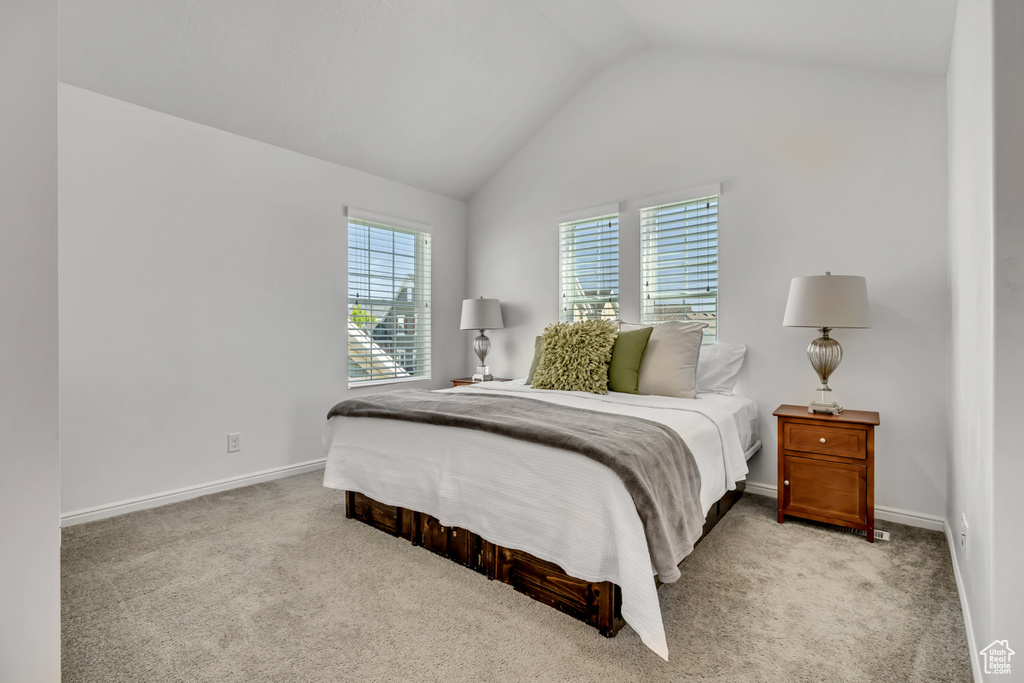 Bedroom with vaulted ceiling, light carpet, and baseboards