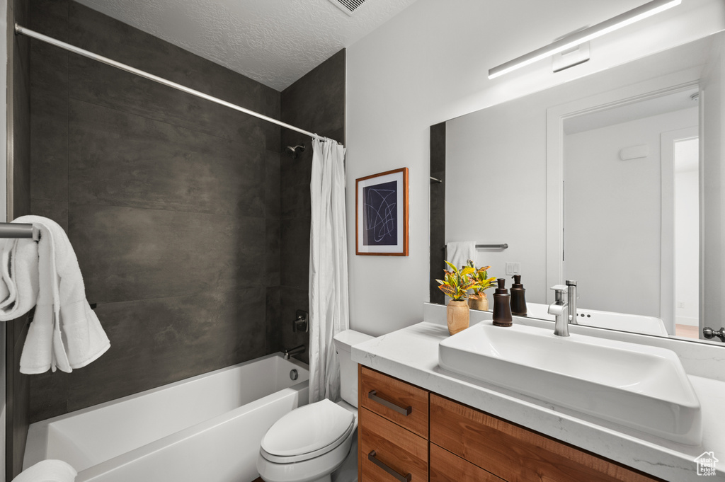 Bathroom featuring vanity, shower / bathtub combination with curtain, toilet, and a textured ceiling