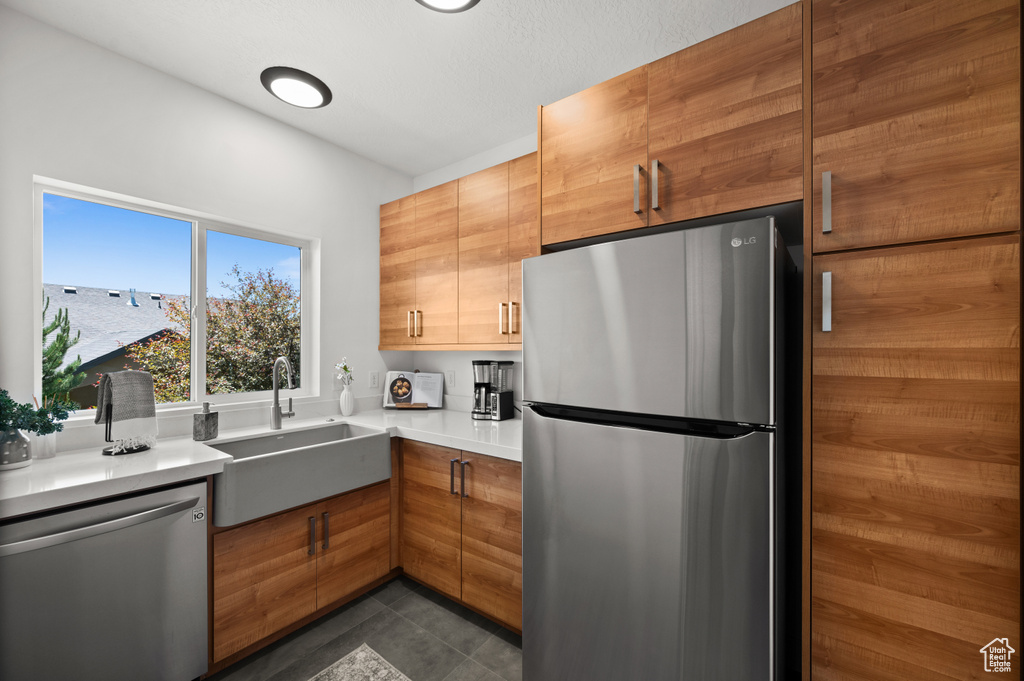 Kitchen with stainless steel appliances, a sink, light countertops, brown cabinetry, and modern cabinets