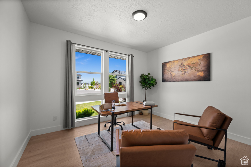 Office space with healthy amount of natural light, light wood-type flooring, baseboards, and a textured ceiling