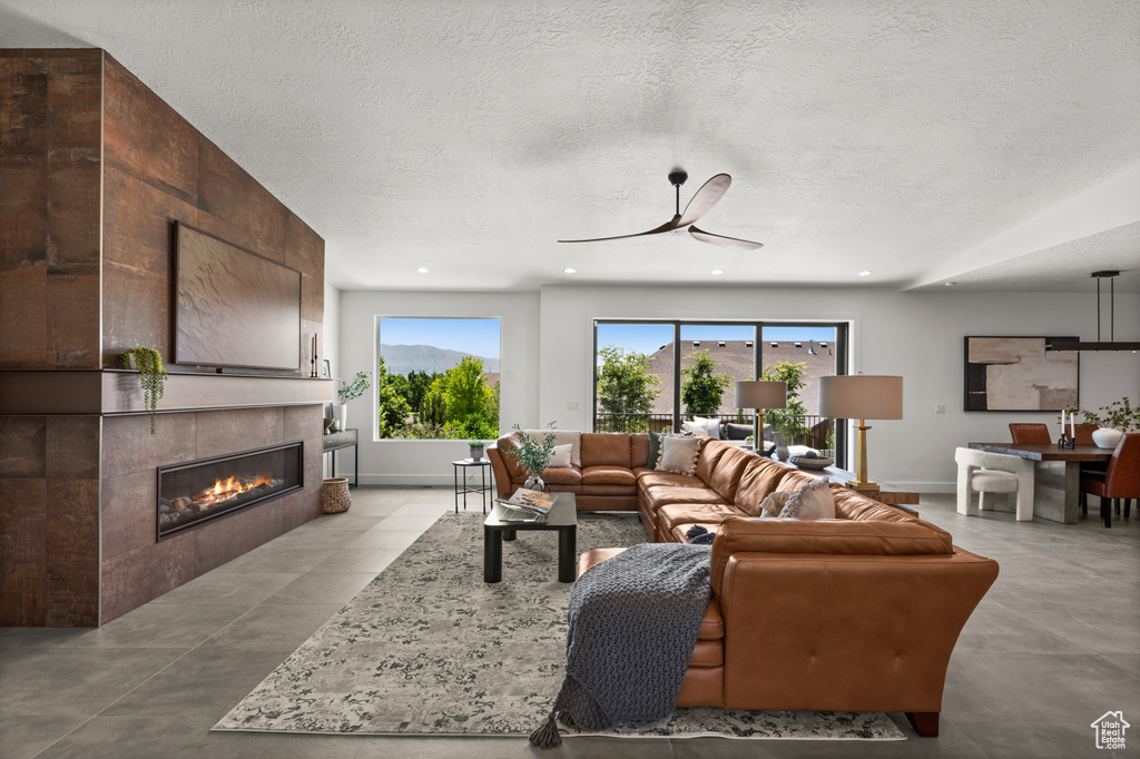 Living room featuring a textured ceiling, a ceiling fan, a tiled fireplace, baseboards, and concrete floors