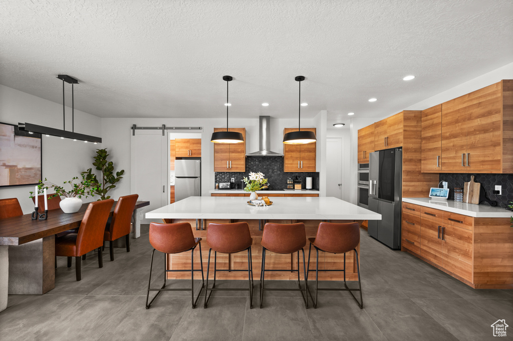 Kitchen with wall chimney exhaust hood, stainless steel appliances, brown cabinets, modern cabinets, and a textured ceiling