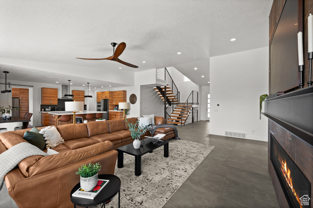 Living room with recessed lighting, stairs, a lit fireplace, ceiling fan, and a textured ceiling