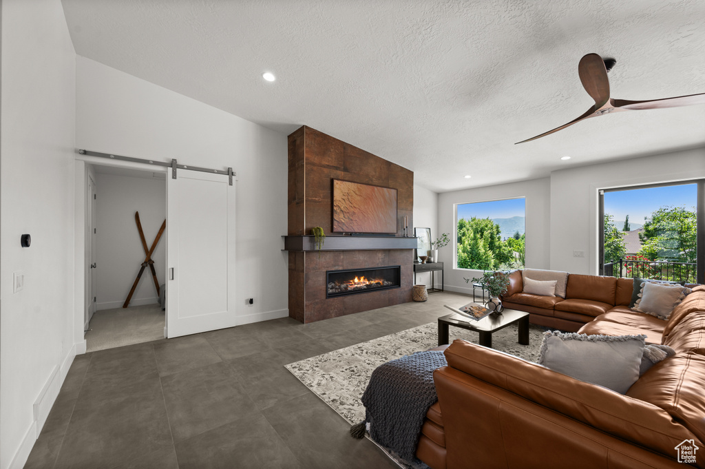 Living room with a barn door, ceiling fan, a tiled fireplace, a textured ceiling, and baseboards