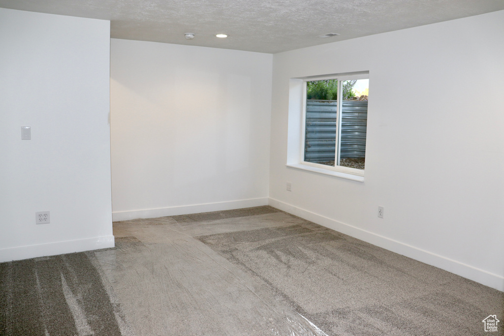 Empty room featuring carpet flooring, baseboards, and a textured ceiling