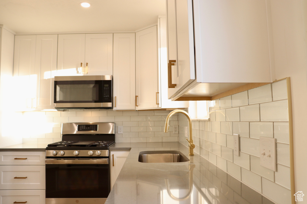 Kitchen featuring appliances with stainless steel finishes, a sink, white cabinets, light countertops, and decorative backsplash