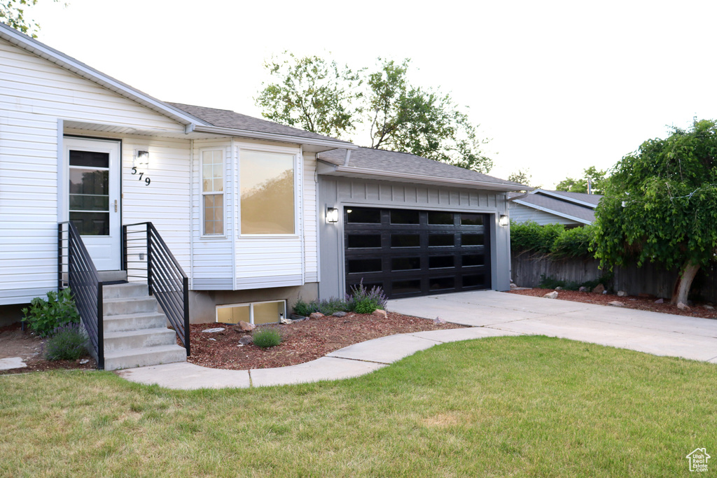 View of front facade with driveway, an attached garage, entry steps, and a front lawn