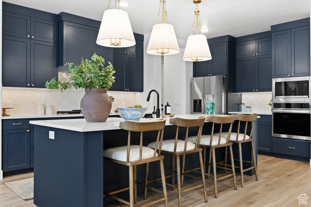 Kitchen featuring stainless steel appliances, blue cabinets, light wood-style flooring, and light countertops