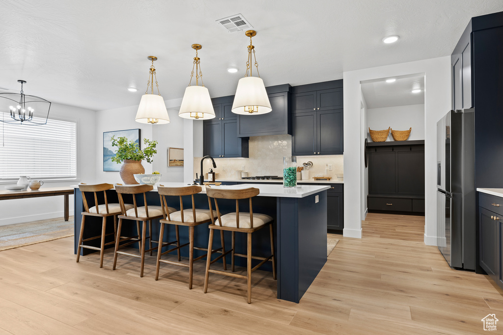 Kitchen featuring stainless steel fridge with ice dispenser, light countertops, backsplash, a center island with sink, and a kitchen breakfast bar