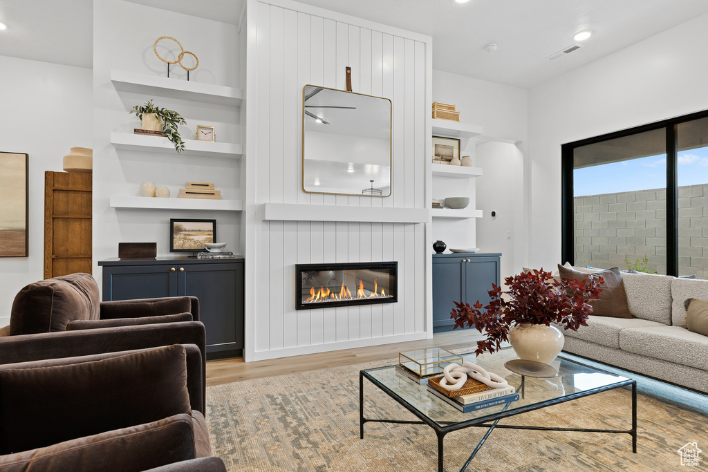 Living room featuring light wood-style flooring, built in features, a glass covered fireplace, and recessed lighting