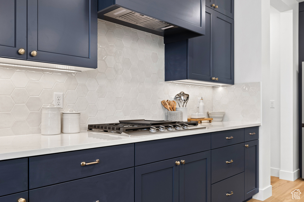 Kitchen with blue cabinetry, premium range hood, backsplash, and stainless steel gas cooktop