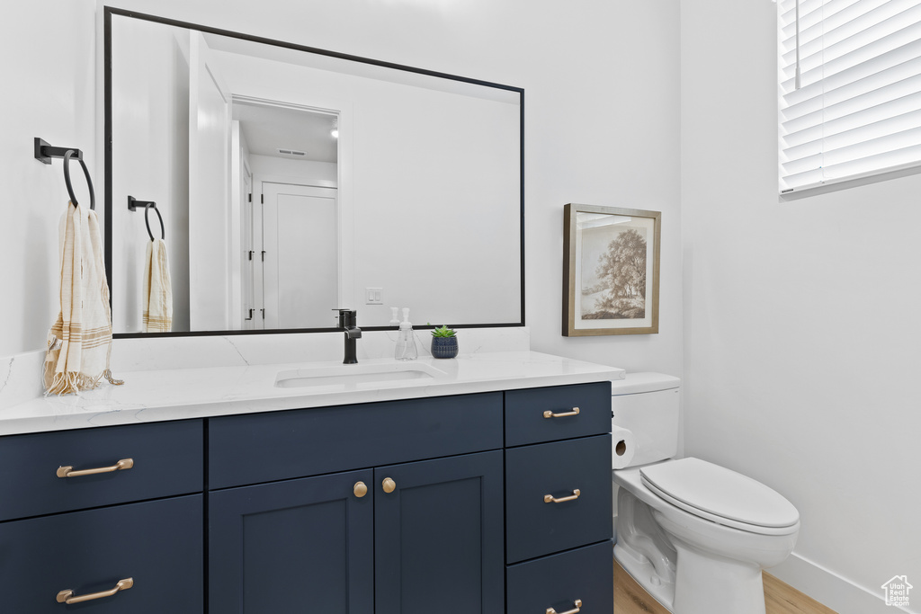 Half bathroom with vanity, toilet, wood finished floors, and baseboards