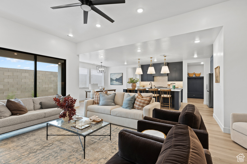 Living room featuring light wood-type flooring, ceiling fan, baseboards, a chandelier, and recessed lighting