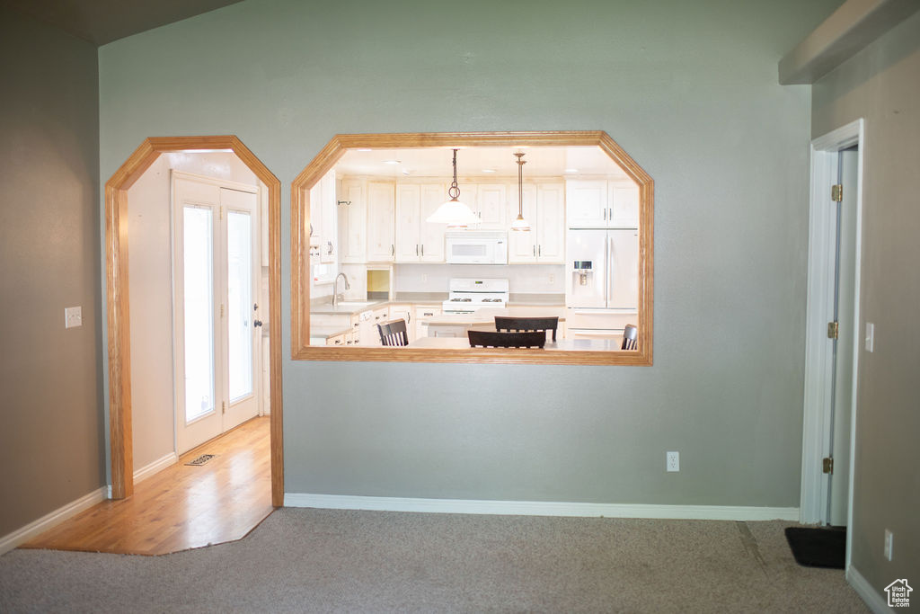 Kitchen with white appliances, carpet, baseboards, pendant lighting, and a sink