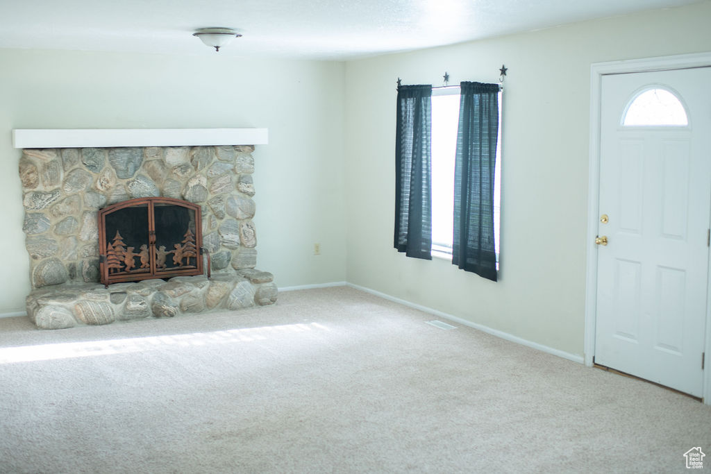Unfurnished living room featuring carpet floors, a stone fireplace, and baseboards