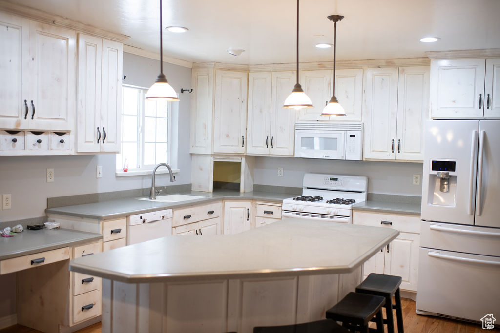 Kitchen with white appliances, a sink, light countertops, a kitchen breakfast bar, and a center island