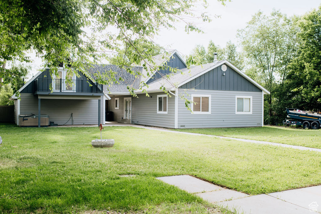 Back of house featuring board and batten siding, a lawn, and a balcony