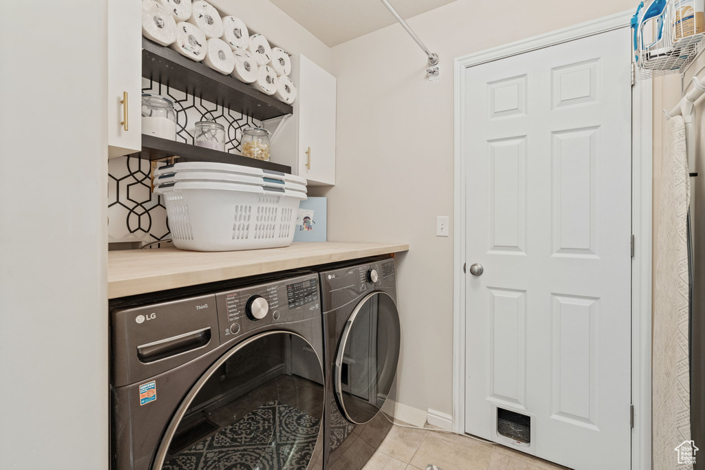 Washroom featuring cabinet space, washing machine and clothes dryer, light tile patterned flooring, and baseboards