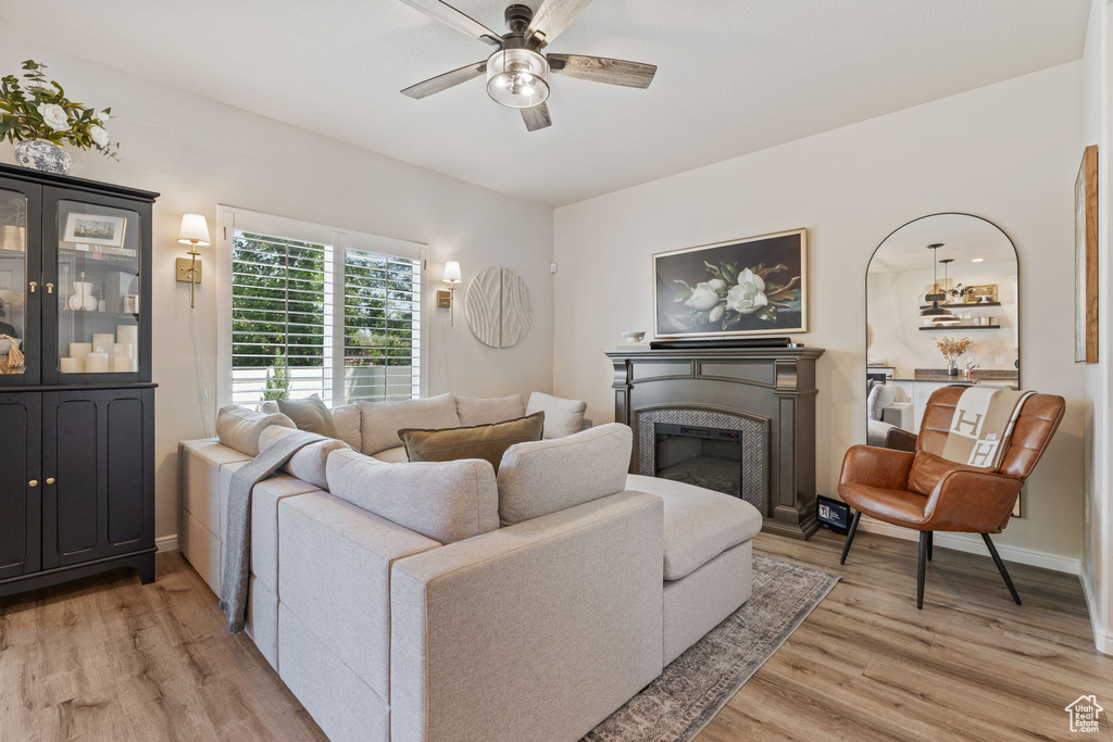 Living area featuring light wood finished floors, ceiling fan, a fireplace, and baseboards