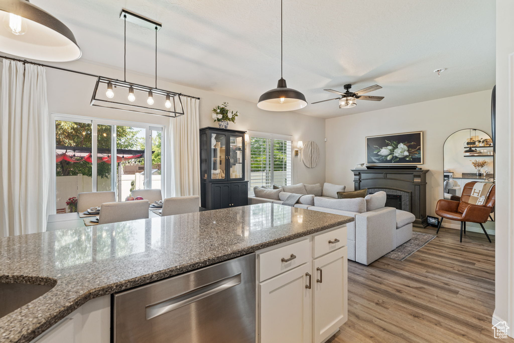 Kitchen featuring dishwasher, a fireplace, white cabinetry, light wood finished floors, and hanging light fixtures