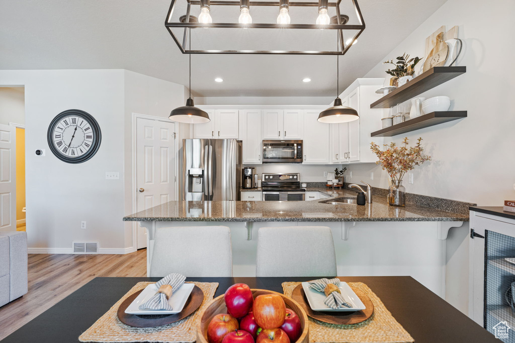 Kitchen featuring stainless steel appliances, a sink, open shelves, light wood-style flooring, and a peninsula