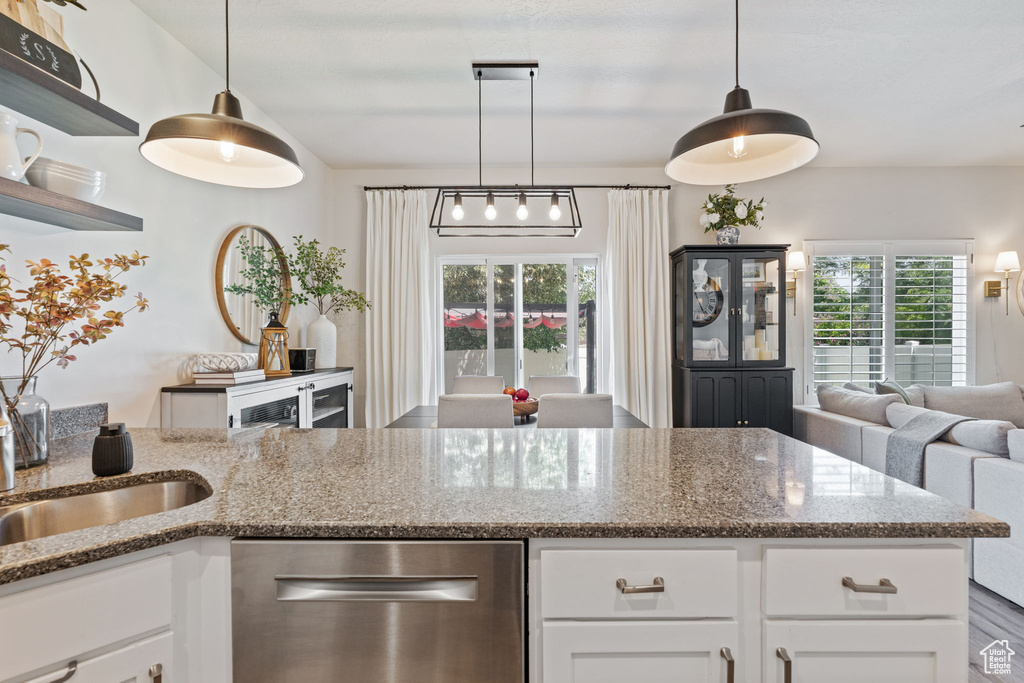 Kitchen featuring stainless steel dishwasher, dark stone counters, white cabinetry, and hanging light fixtures