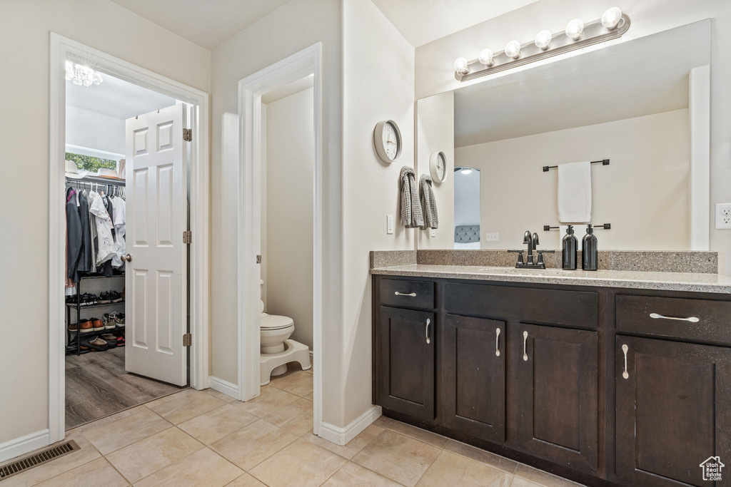 Full bathroom with vanity, baseboards, toilet, a walk in closet, and tile patterned floors