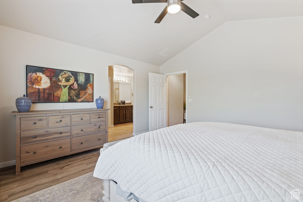 Bedroom with light wood-style flooring, arched walkways, ceiling fan, ensuite bath, and high vaulted ceiling