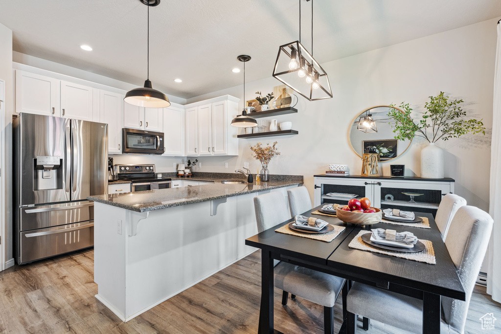 Kitchen with appliances with stainless steel finishes, a peninsula, light wood-style flooring, white cabinets, and dark stone countertops