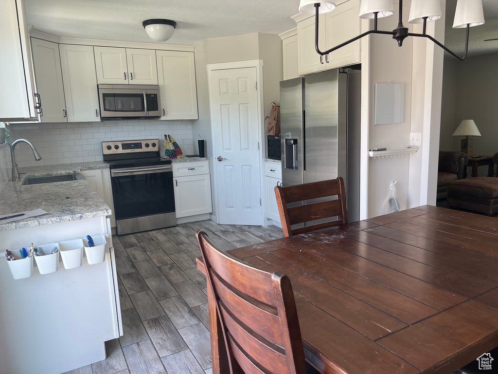Kitchen featuring stainless steel appliances, a sink, decorative backsplash, dark wood finished floors, and light stone counters