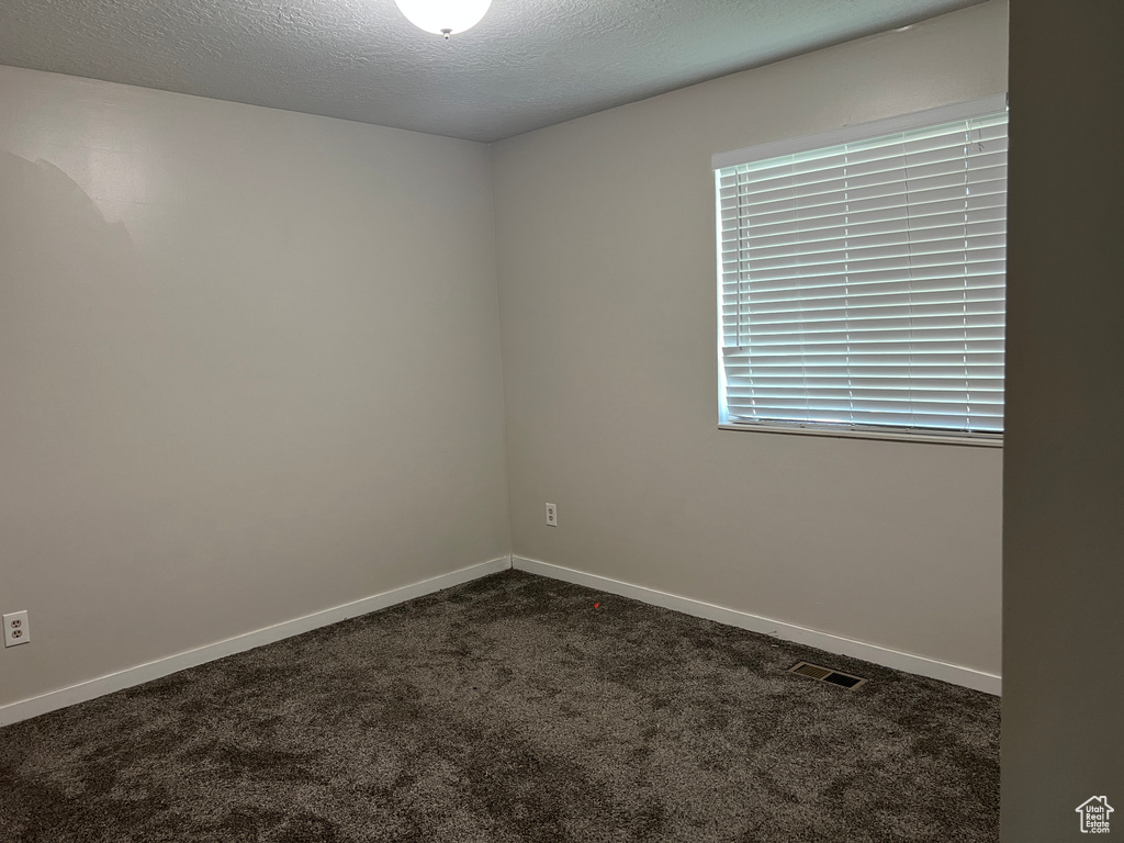 Unfurnished room featuring dark colored carpet, baseboards, and a textured ceiling