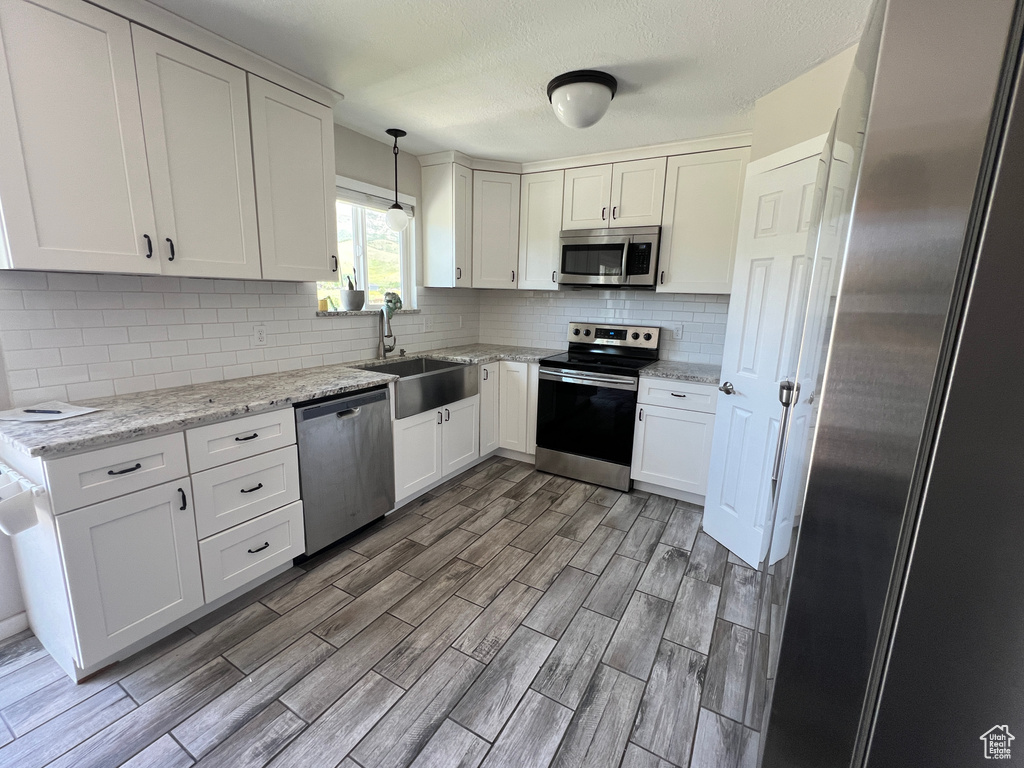 Kitchen with stainless steel appliances, a sink, light wood-type flooring, decorative backsplash, and a textured ceiling
