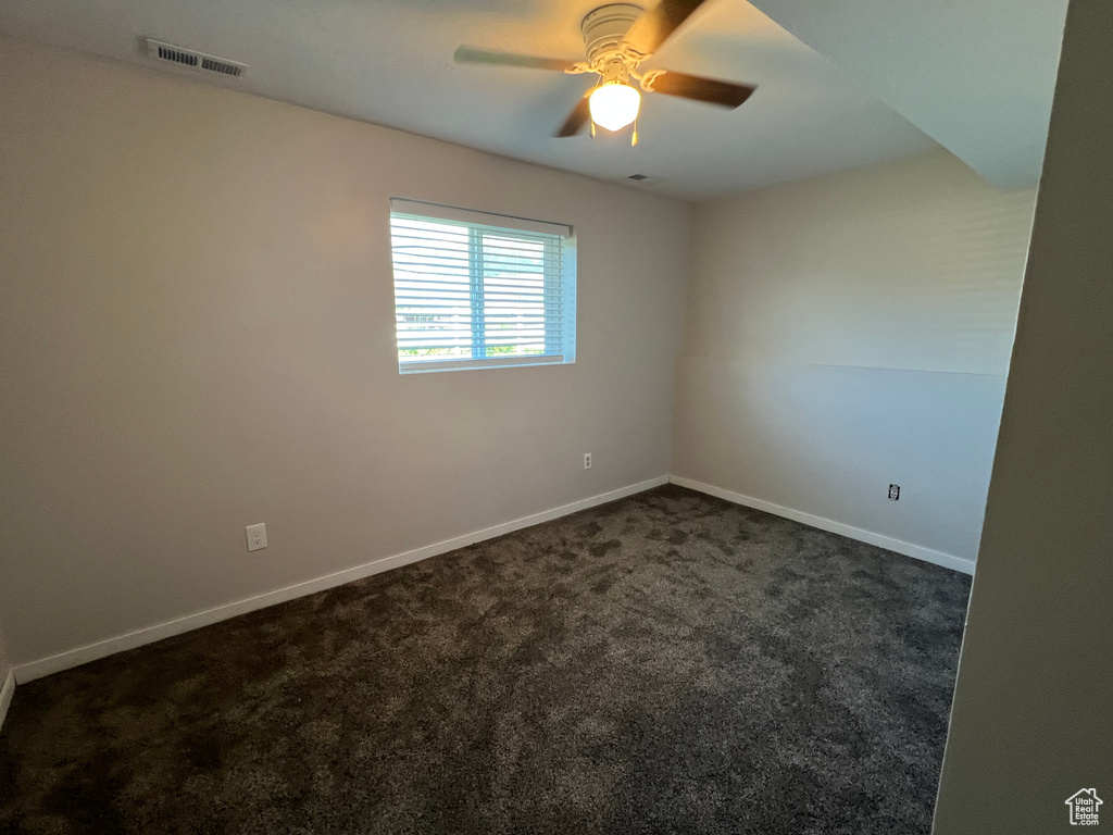 Empty room with dark colored carpet, a ceiling fan, and baseboards