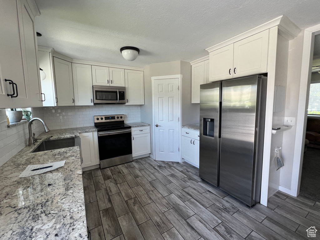 Kitchen featuring appliances with stainless steel finishes, a sink, wood tiled floors, tasteful backsplash, and light stone countertops