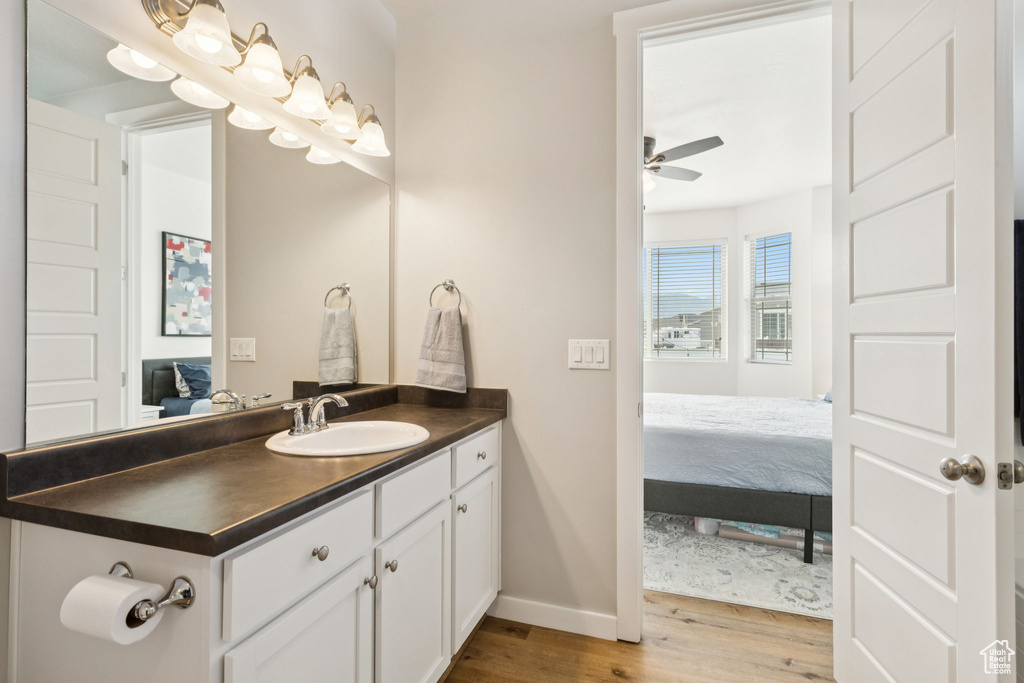 Bathroom featuring connected bathroom, wood finished floors, vanity, baseboards, and a ceiling fan