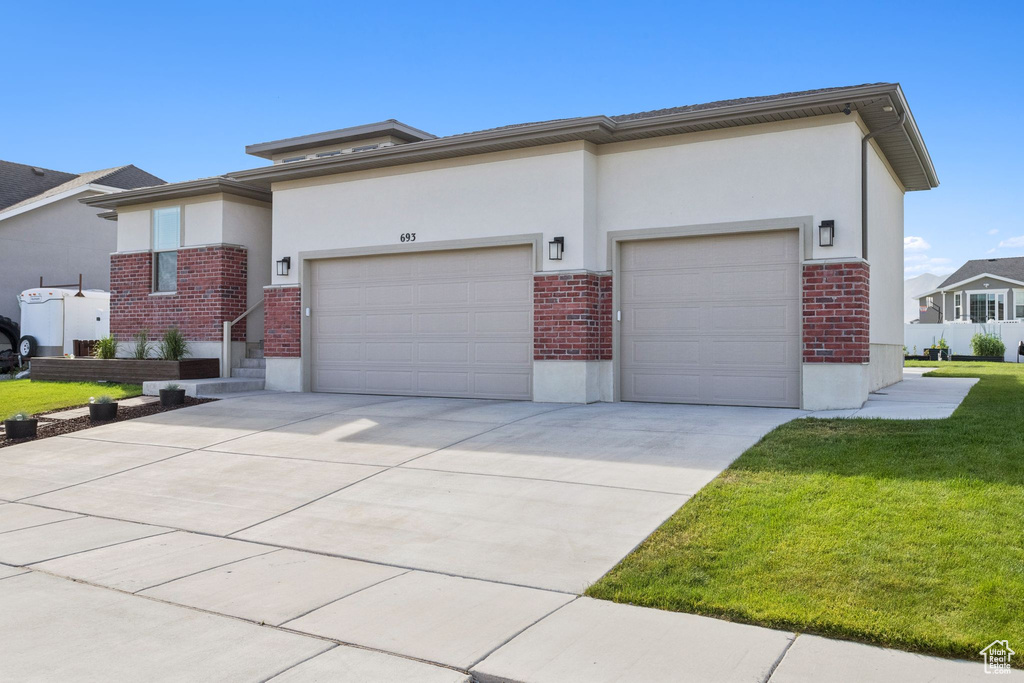 Prairie-style house with brick siding, a garage, a front lawn, concrete driveway, and stucco siding