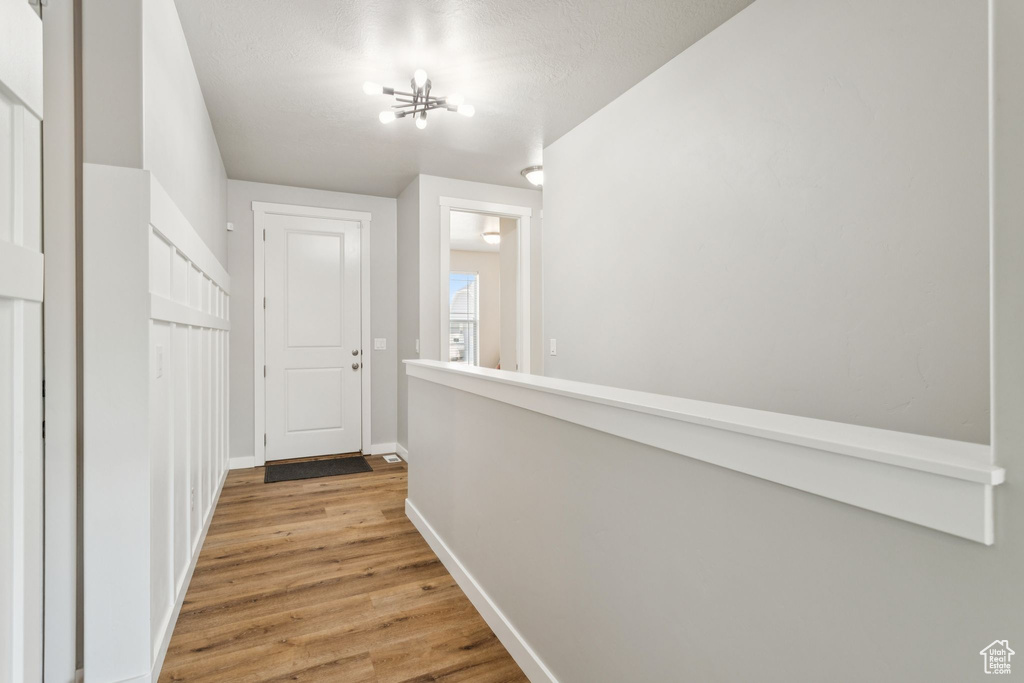 Hall featuring baseboards, light wood-type flooring, and a chandelier