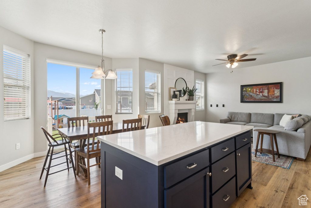 Kitchen with light wood-style floors, light countertops, a warm lit fireplace, a center island, and a ceiling fan