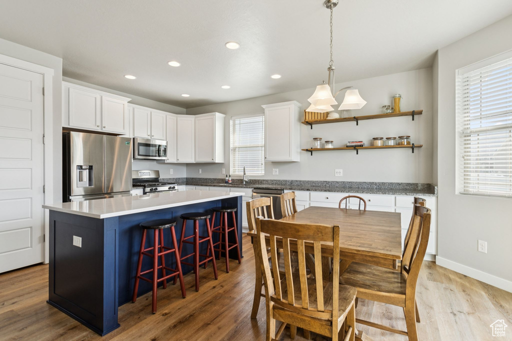 Kitchen featuring stainless steel appliances, white cabinets, a sink, a kitchen island, and wood finished floors
