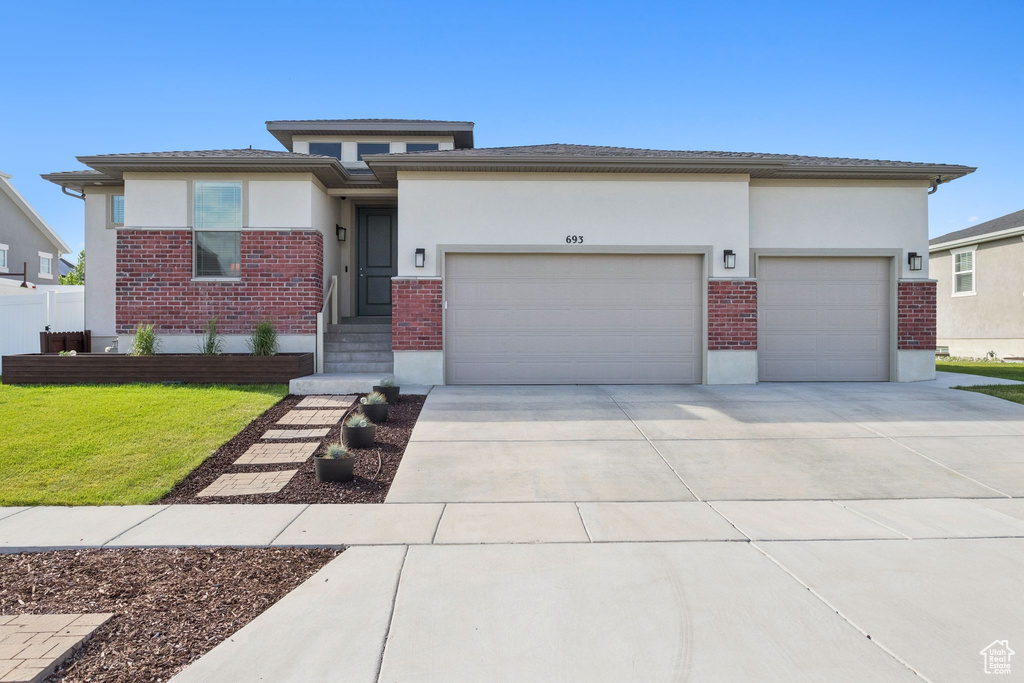 Prairie-style home with a garage, brick siding, stucco siding, and driveway