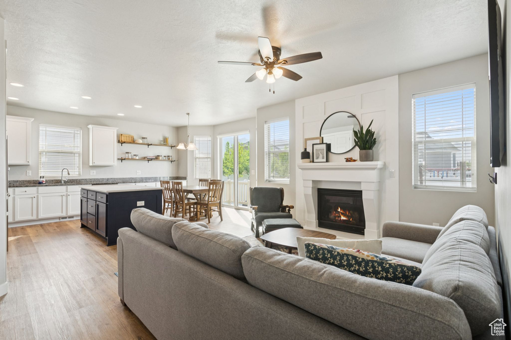 Living area with ceiling fan, light wood-style floors, a glass covered fireplace, and recessed lighting