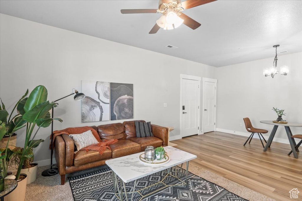 Living room with a chandelier, a ceiling fan, baseboards, and light wood-style floors