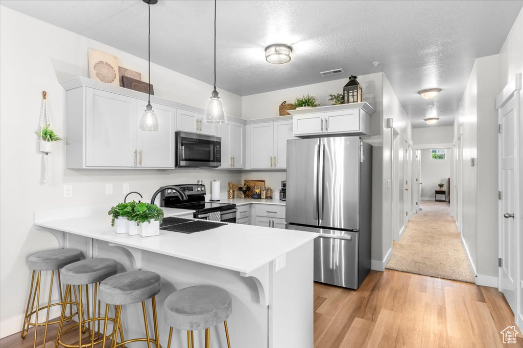 Kitchen with stainless steel appliances, a peninsula, light countertops, a breakfast bar area, and light wood-style floors
