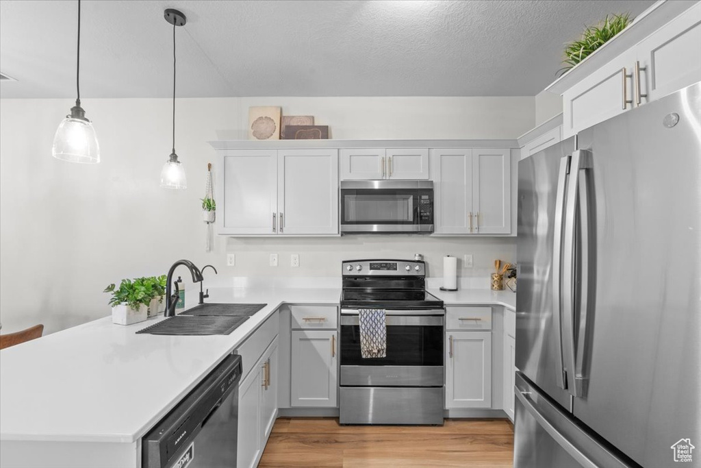 Kitchen with stainless steel appliances, a sink, a peninsula, light countertops, and light wood-type flooring
