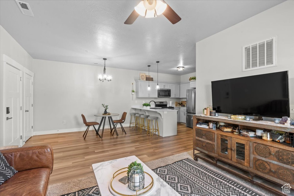 Living room featuring light wood-style floors, ceiling fan, a chandelier, and baseboards