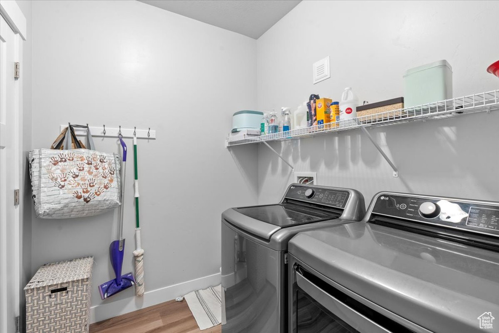 Washroom with washing machine and clothes dryer, wood finished floors, and baseboards