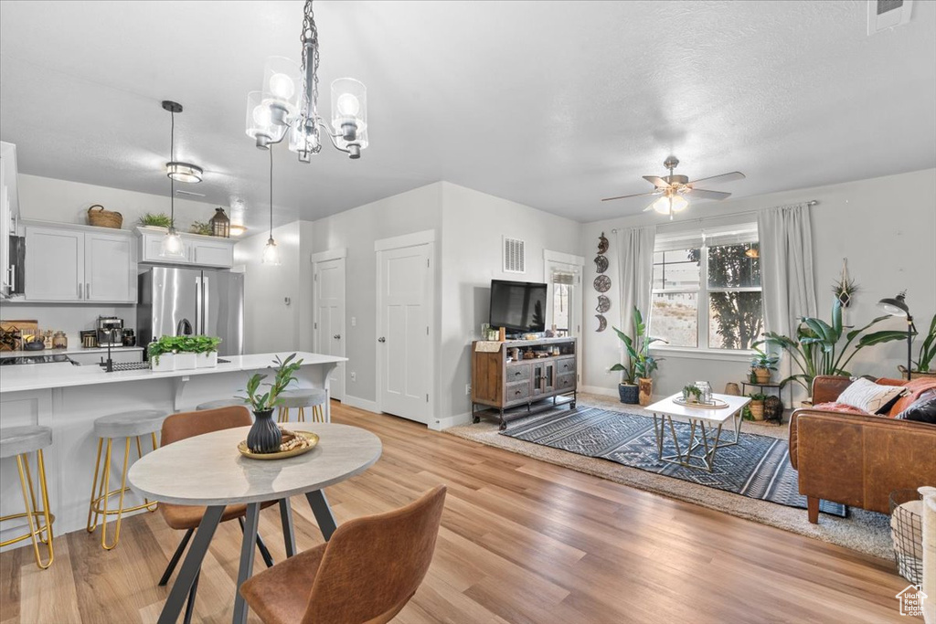 Living room with light wood-style flooring, a ceiling fan, a chandelier, and baseboards