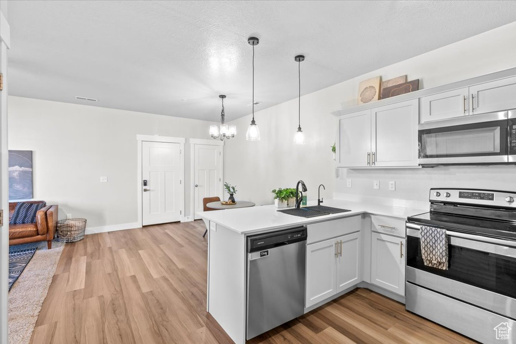 Kitchen with stainless steel appliances, a sink, a peninsula, and light wood finished floors