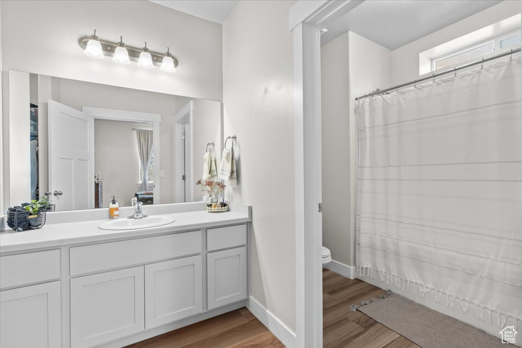 Full bathroom with vanity, wood finished floors, toilet, baseboards, and curtained shower